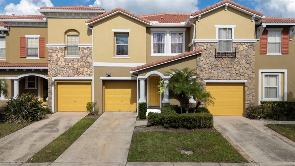A multi-story townhouse exterior features tan stucco, stone accents, yellow garage doors, and a tiled roof — 3008 SEAVIEW CASTLE DRIVE, KISSIMMEE, FL