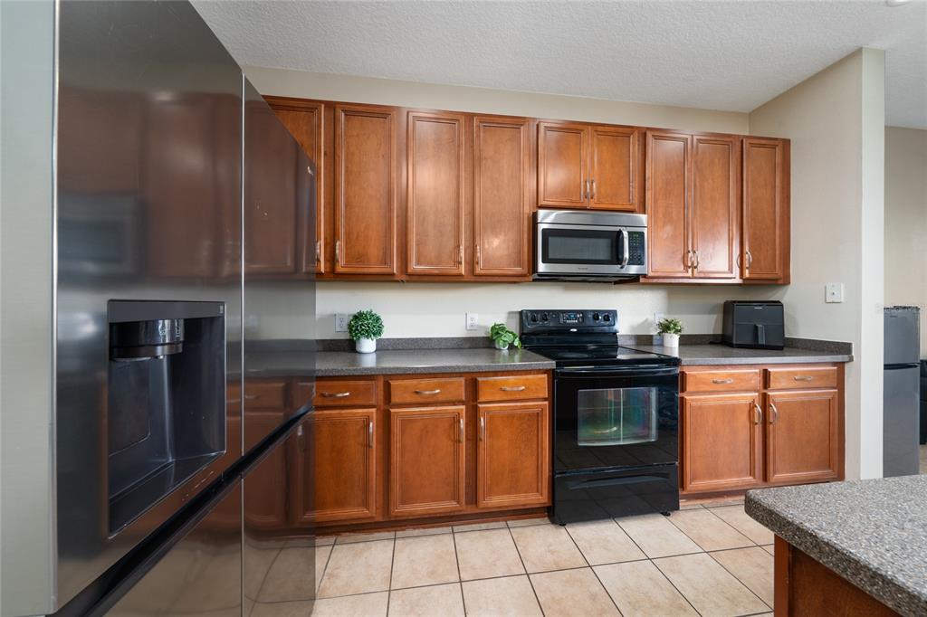 A kitchen features wood cabinets, dark countertops, stainless steel appliances, and tile flooring — 3008 SEAVIEW CASTLE DRIVE, KISSIMMEE, FL