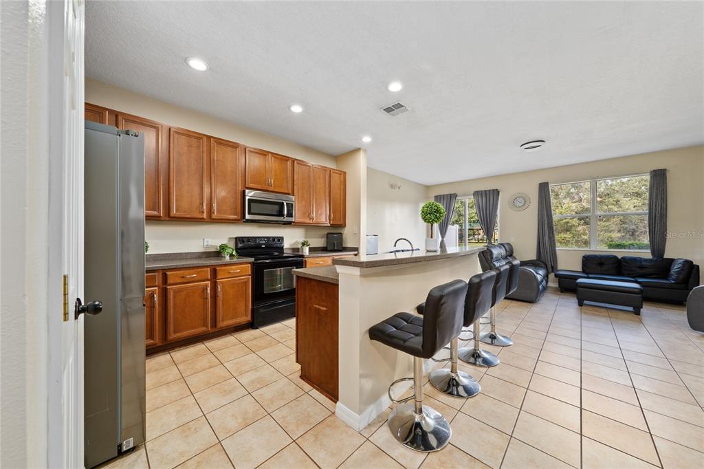 A kitchen with wood cabinets and a breakfast bar opens into a living area — 3008 SEAVIEW CASTLE DRIVE, KISSIMMEE, FL