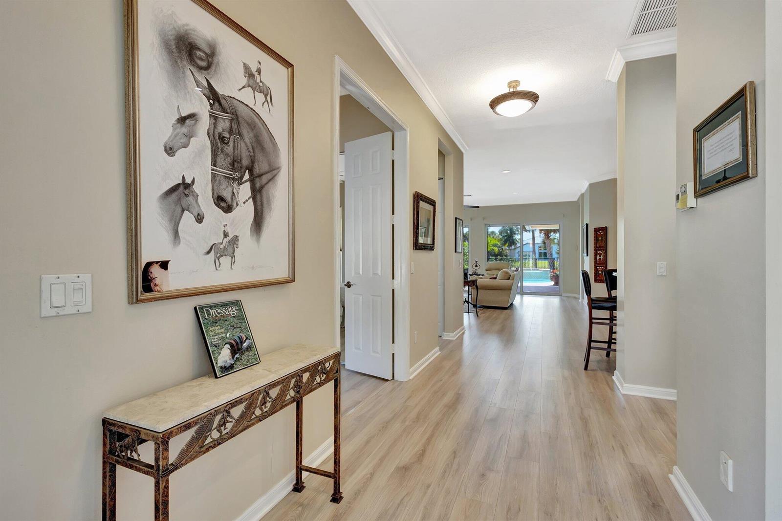 A hallway with light wood floors leads to a living area with a pool view — 2941 Twin Oaks Way, Wellington FL 33414, WELLINGTON, FL
