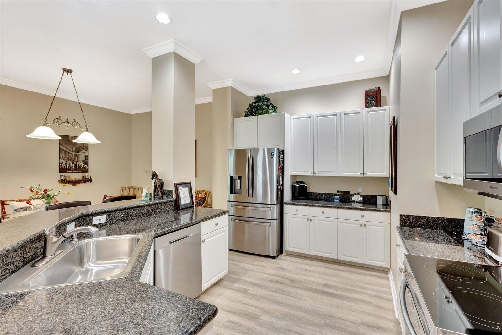 A kitchen features white cabinets, stainless steel appliances, dark granite countertops, and light wood flooring — 2941 Twin Oaks Way, Wellington FL 33414, WELLINGTON, FL