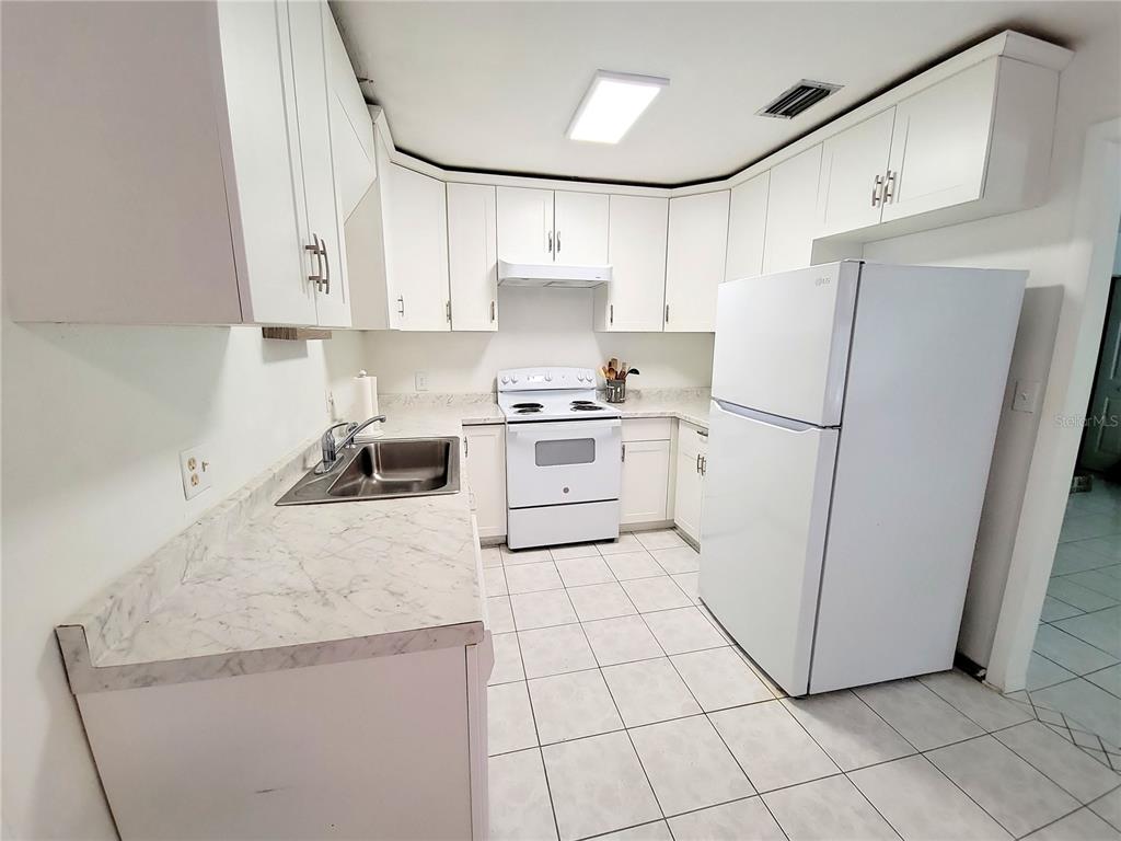 A kitchen features white cabinets, white appliances, and marble-patterned laminate countertops over tiled flooring — 3301 NW 19TH STREET, GAINESVILLE, FL