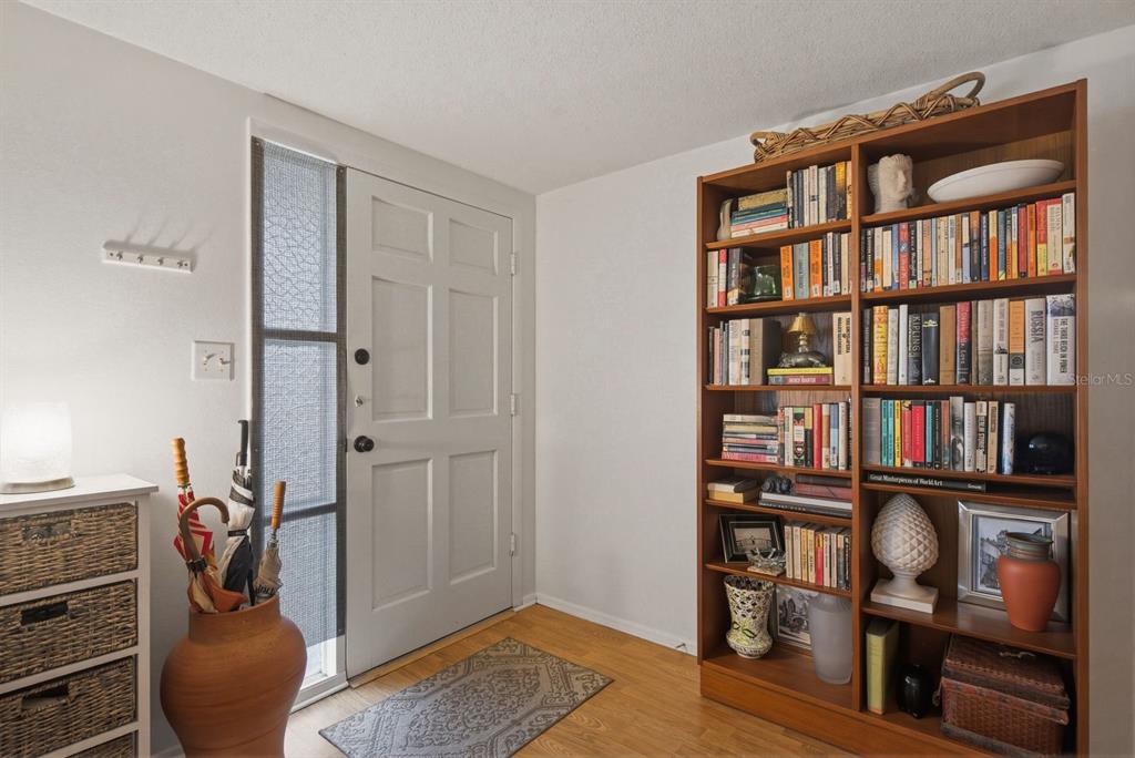 An entryway features a white front door, a tall wooden bookshelf, and light wood flooring — 1958 ESSEX DRIVE, HOLIDAY, FL