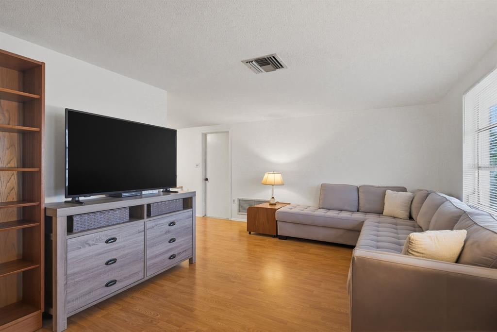 A living room features a television on a wooden dresser, a sectional sofa, and flooring — 1958 ESSEX DRIVE, HOLIDAY, FL