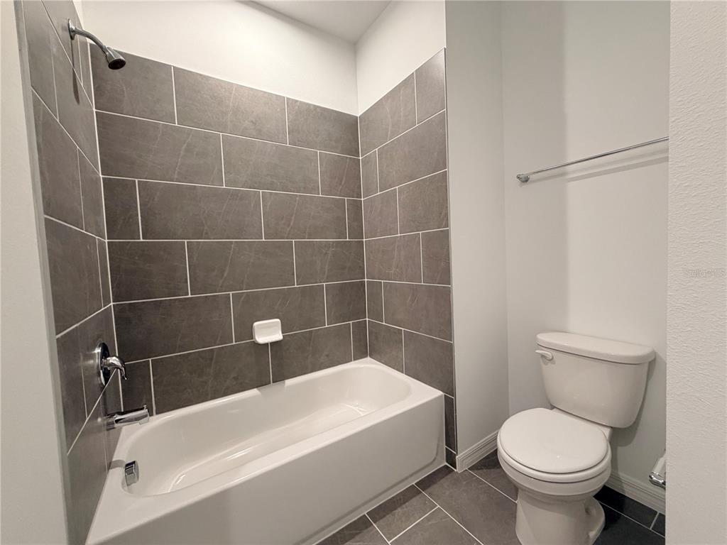 A bathroom features a gray tiled tub-shower combination, a white toilet, and dark floor tiles — 449 BELMOND DRIVE, DEBARY, FL