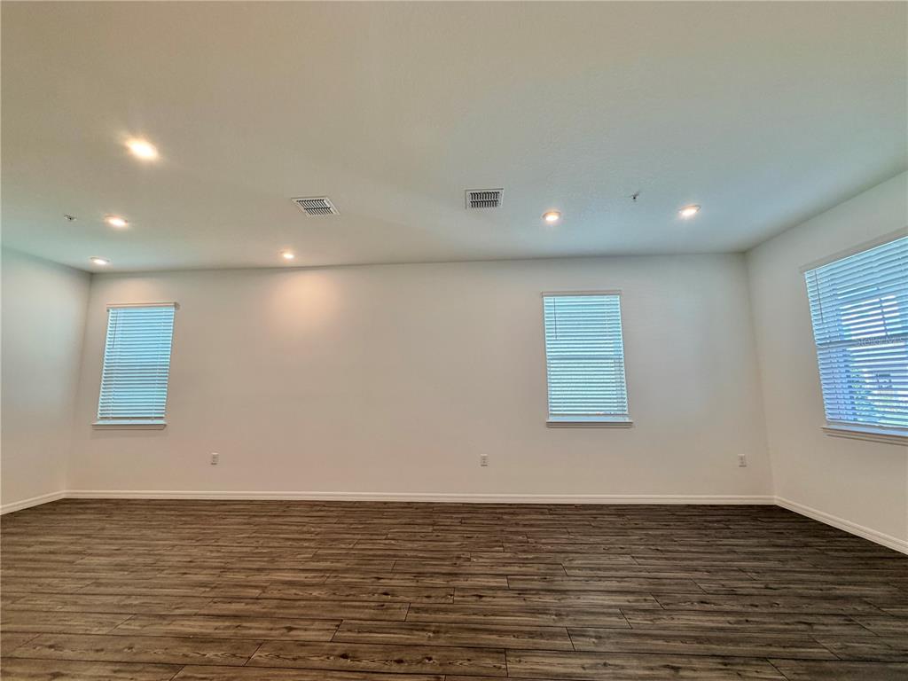 An empty room features white walls, dark wood-look flooring, recessed lighting, and three windows — 449 BELMOND DRIVE, DEBARY, FL