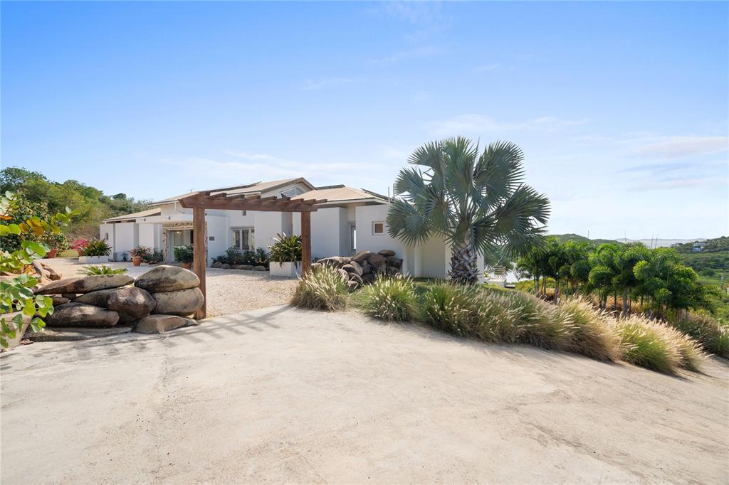 A modern house with a wooden pergola entrance, stone landscaping, and a large palm tree — 11 BARRIO FRAILES, CULEBRA, PR