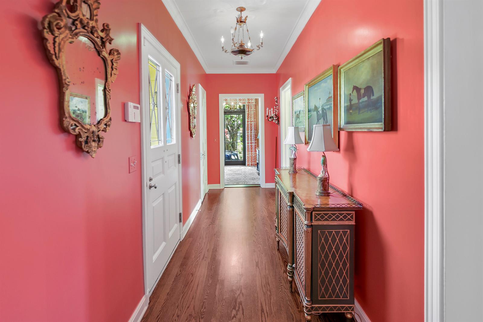 A hallway with coral walls, hardwood floors, a wooden console table, and framed artwork — 250 Algoma Road, Palm Beach FL 33480, PALM BEACH, FL