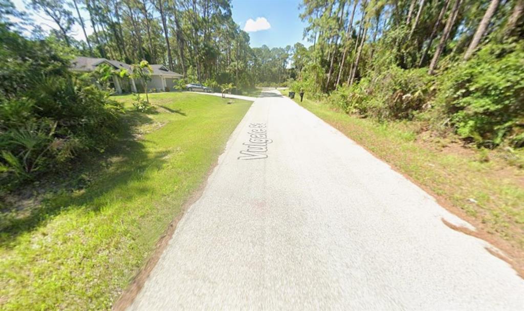 A paved street runs through a wooded residential area with a house on the left — VULGATE STREET, NORTH PORT, FL