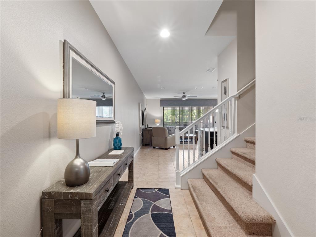 A hallway features a wooden console table, a mirror, and stairs leading to an upper level — 8867 GENEVE COURT, KISSIMMEE, FL