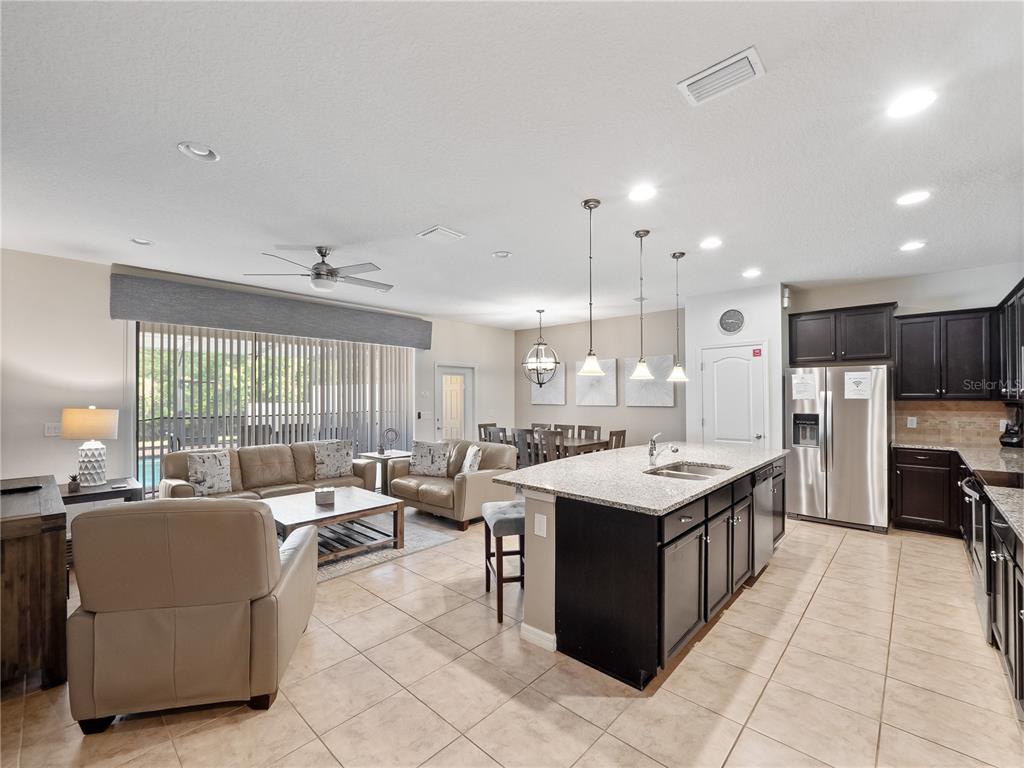 An open-concept living room and kitchen featuring tile floors, dark cabinetry, and a granite island — 8867 GENEVE COURT, KISSIMMEE, FL