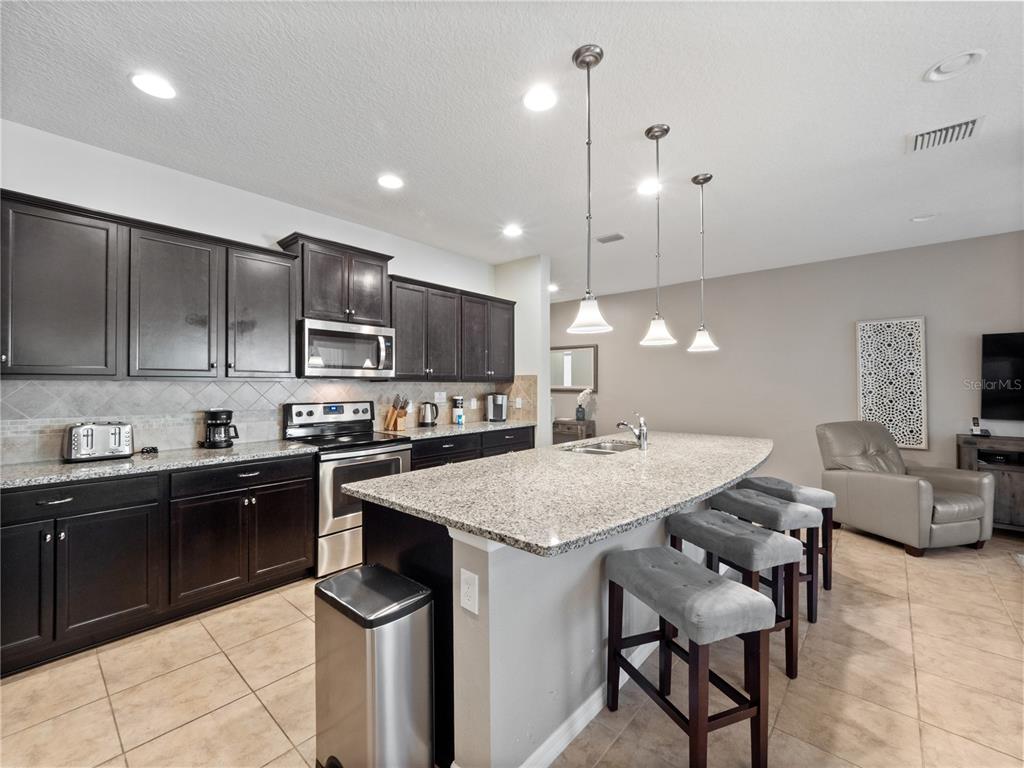 A kitchen features dark wood cabinets, granite countertops, a center island, and three bar stools — 8867 GENEVE COURT, KISSIMMEE, FL