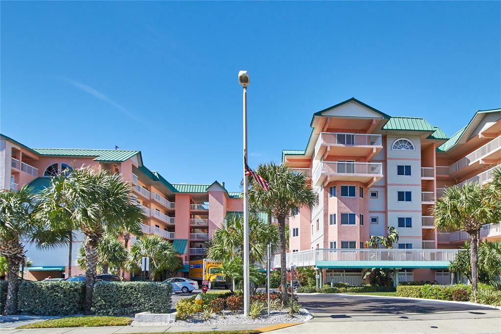A multi-story pink apartment complex with green roofs and palm trees under a clear sky — 18400 GULF BOULEVARD UNIT 1206, INDIAN SHORES, FL