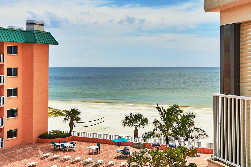 An elevated view of a beachside patio with lounge chairs, palm trees, and the ocean — 18400 GULF BOULEVARD UNIT 1206, INDIAN SHORES, FL