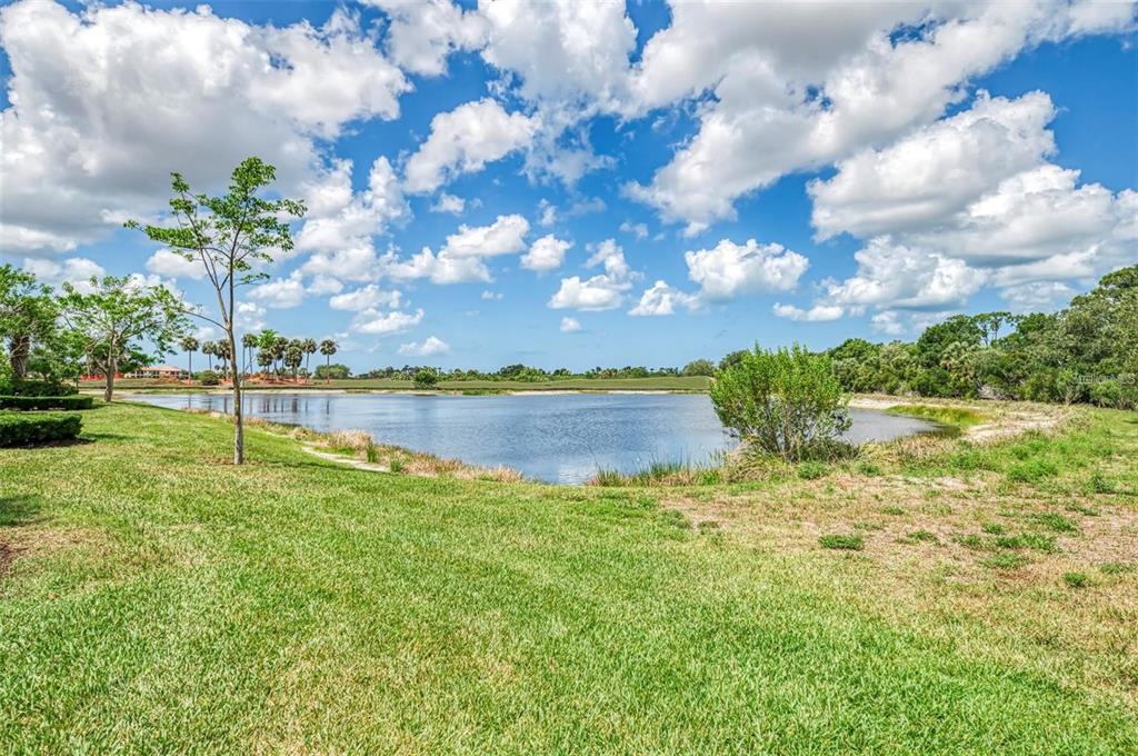 A grassy lawn leads to a pond with trees and a blue sky above — 23321 AWABUKI DRIVE UNIT 8-102, VENICE, FL