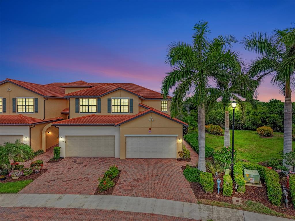 A two-story stucco townhouse with a red tile roof and a brick paver driveway — 23321 AWABUKI DRIVE UNIT 8-102, VENICE, FL