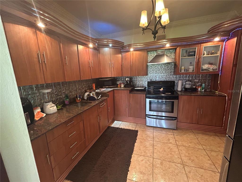 A kitchen features wood cabinets, a stainless steel stove, and a metallic tile backsplash — 545 SECTOR TORO, COAMO, PR