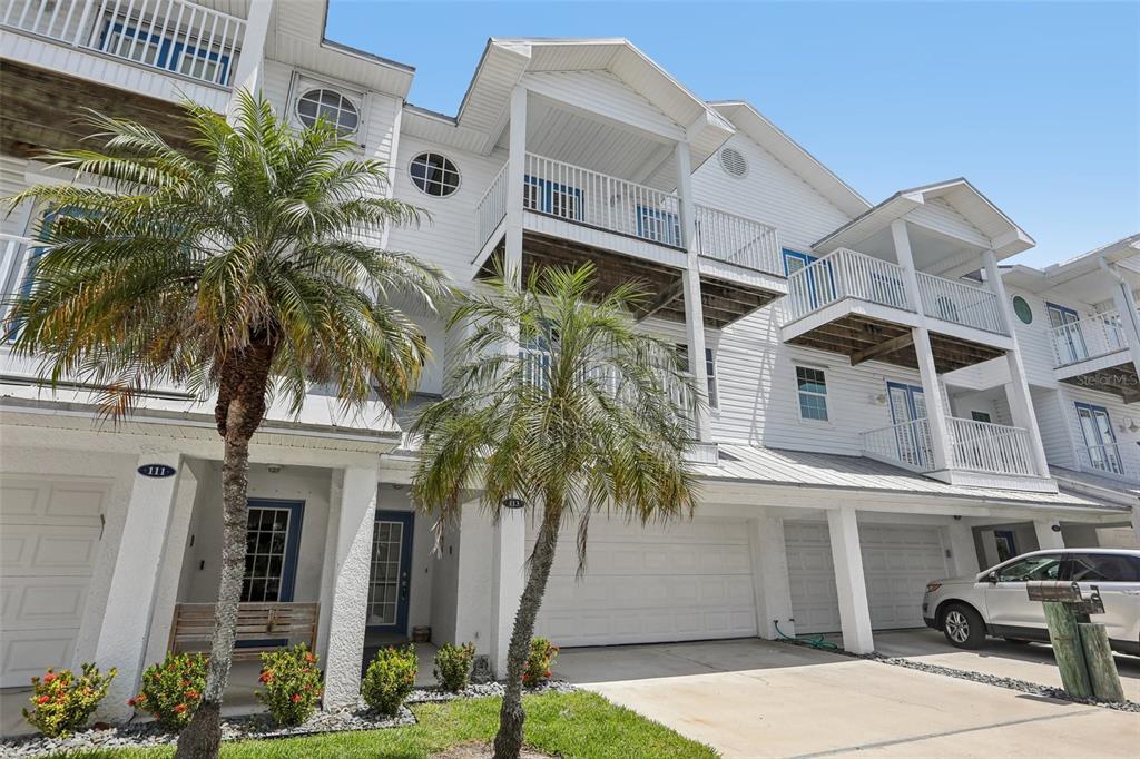 A three-story white townhouse with balconies, a two-car garage, and palm trees in front — 113 YACHT CLUB CIRCLE, NORTH REDINGTON BEACH, FL