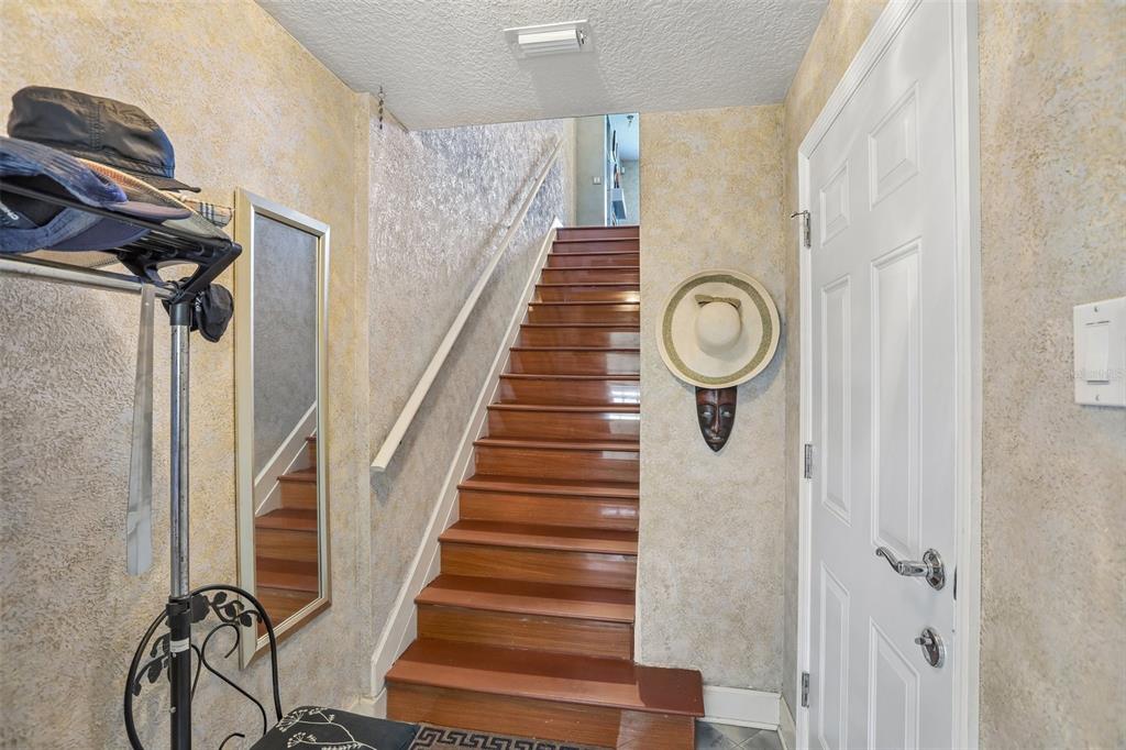 A staircase with wooden treads leads upward between textured walls in a home entryway — 113 YACHT CLUB CIRCLE, NORTH REDINGTON BEACH, FL