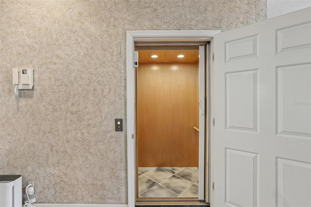 An open residential elevator with wood-paneled walls sits beside a white door on a textured wall — 113 YACHT CLUB CIRCLE, NORTH REDINGTON BEACH, FL