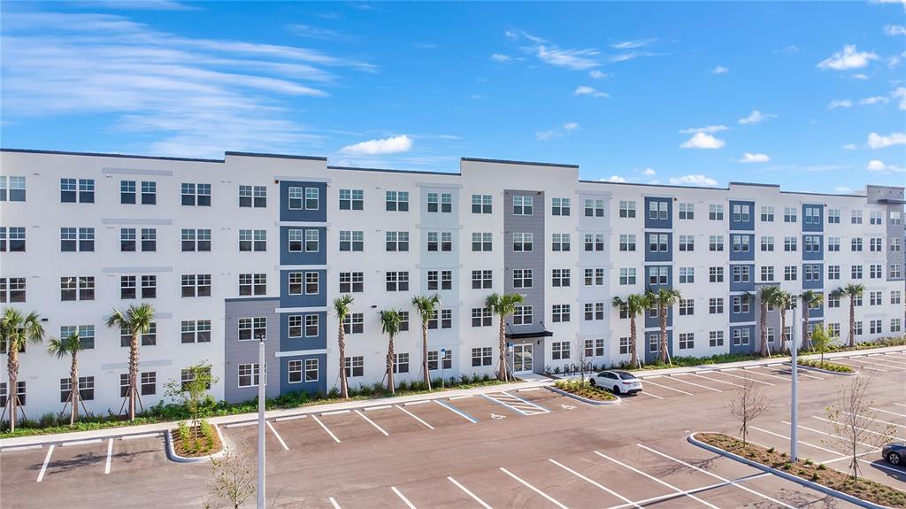 A multi-story apartment building with a parking lot in the foreground under a blue sky — 5579 MILLENIA PARK BOULEVARD UNIT 106, ORLANDO, FL
