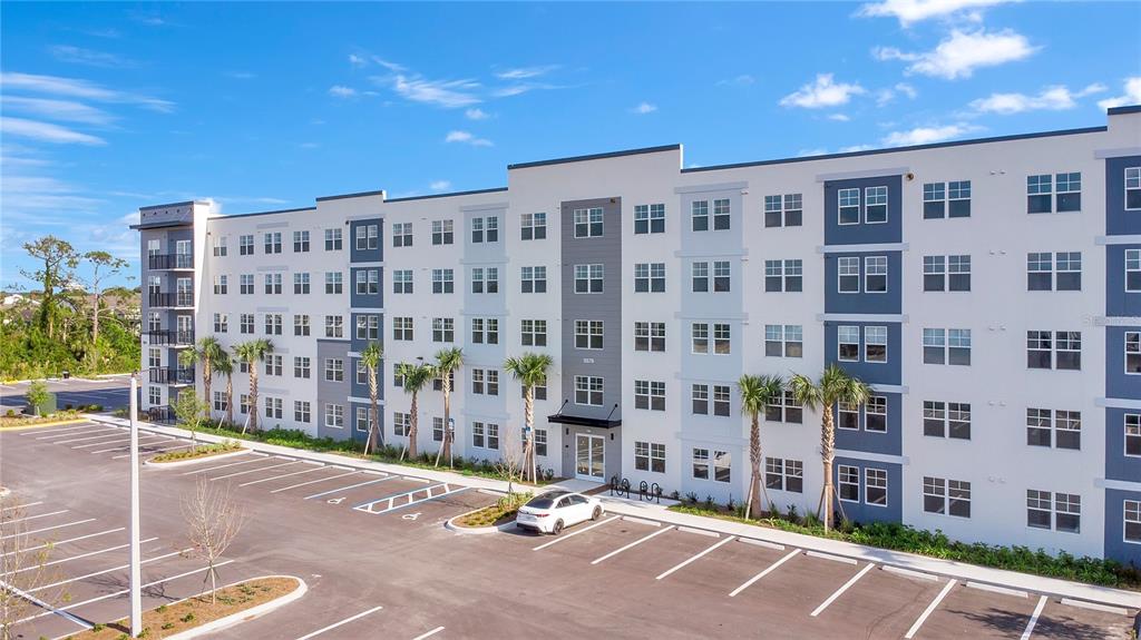 A multi-story apartment building features a white facade with blue accents and a parking lot — 5579 MILLENIA PARK BOULEVARD UNIT 106, ORLANDO, FL