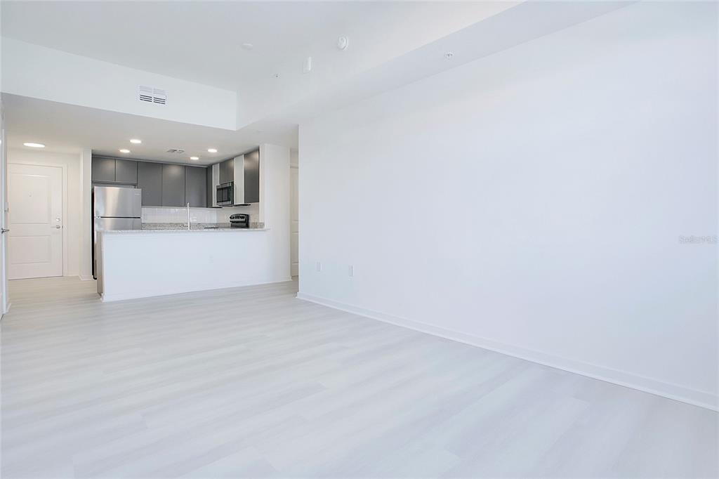 A bright, open-concept living area features light wood-look flooring and an adjacent kitchen with gray cabinets — 5579 MILLENIA PARK BOULEVARD UNIT 106, ORLANDO, FL