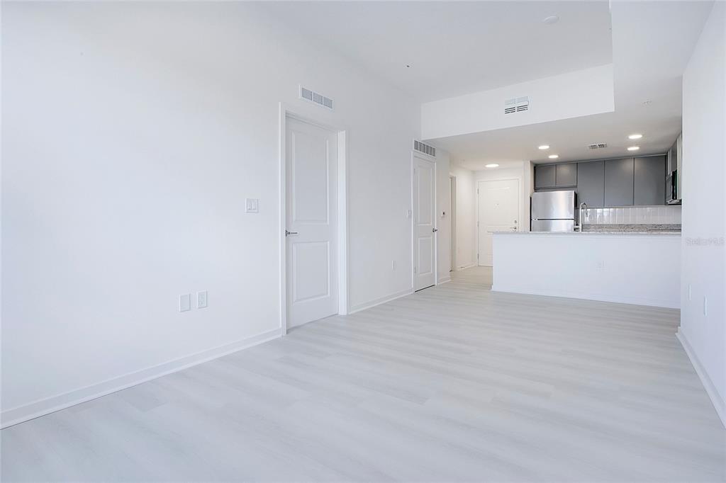 An interior view of an apartment featuring light wood flooring, white walls, and a kitchen — 5579 MILLENIA PARK BOULEVARD UNIT 106, ORLANDO, FL