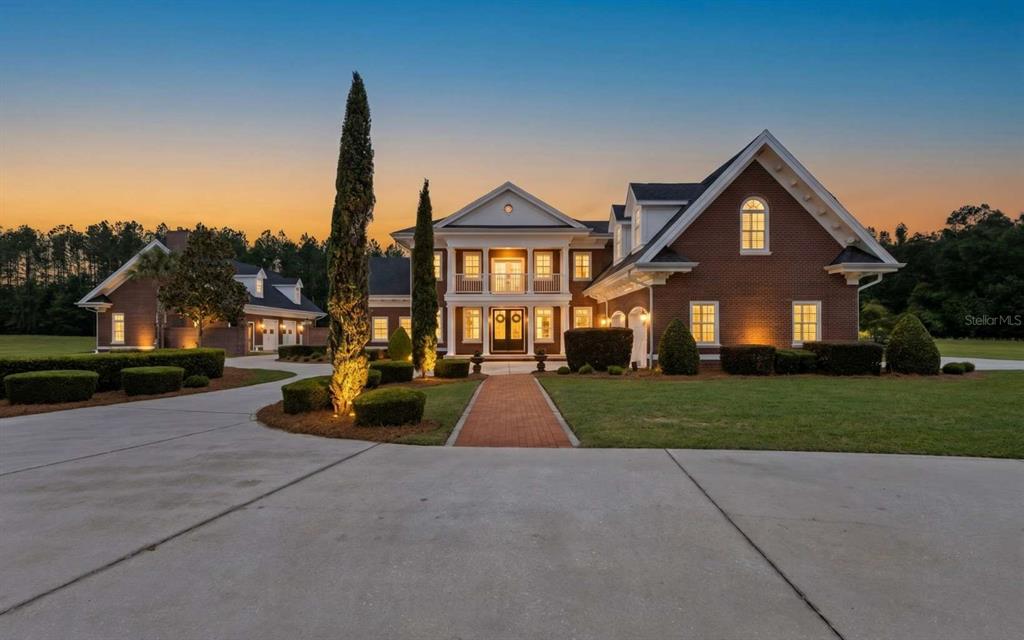 A large two-story brick house with a columned portico and a detached garage at dusk — 537 SW WINDSOR DRIVE, LAKE CITY, FL