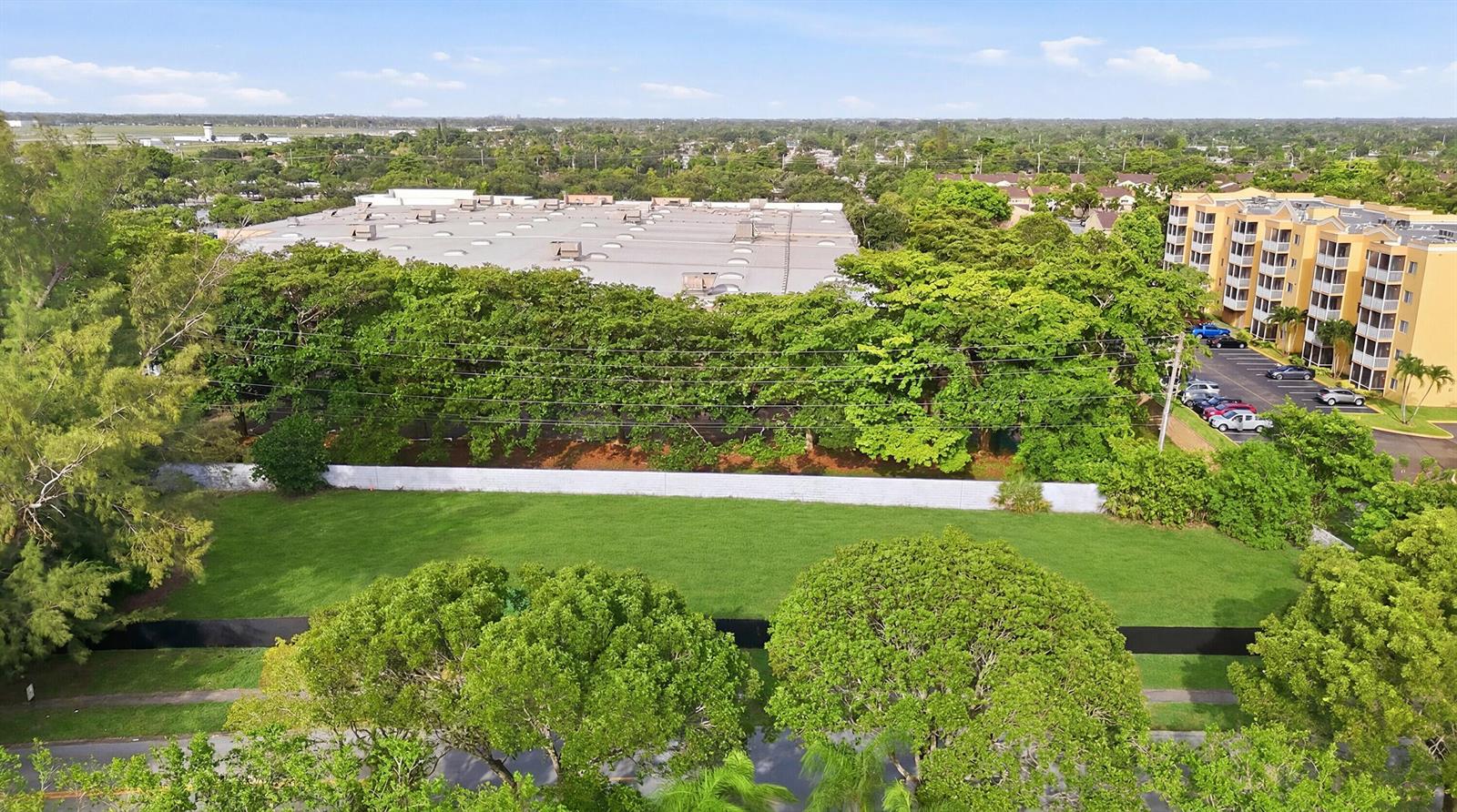 An aerial view shows a grassy lot bordered by trees, a wall, and nearby buildings — 1800 N Sherman Circle, Miramar FL 33025, MIRAMAR, FL