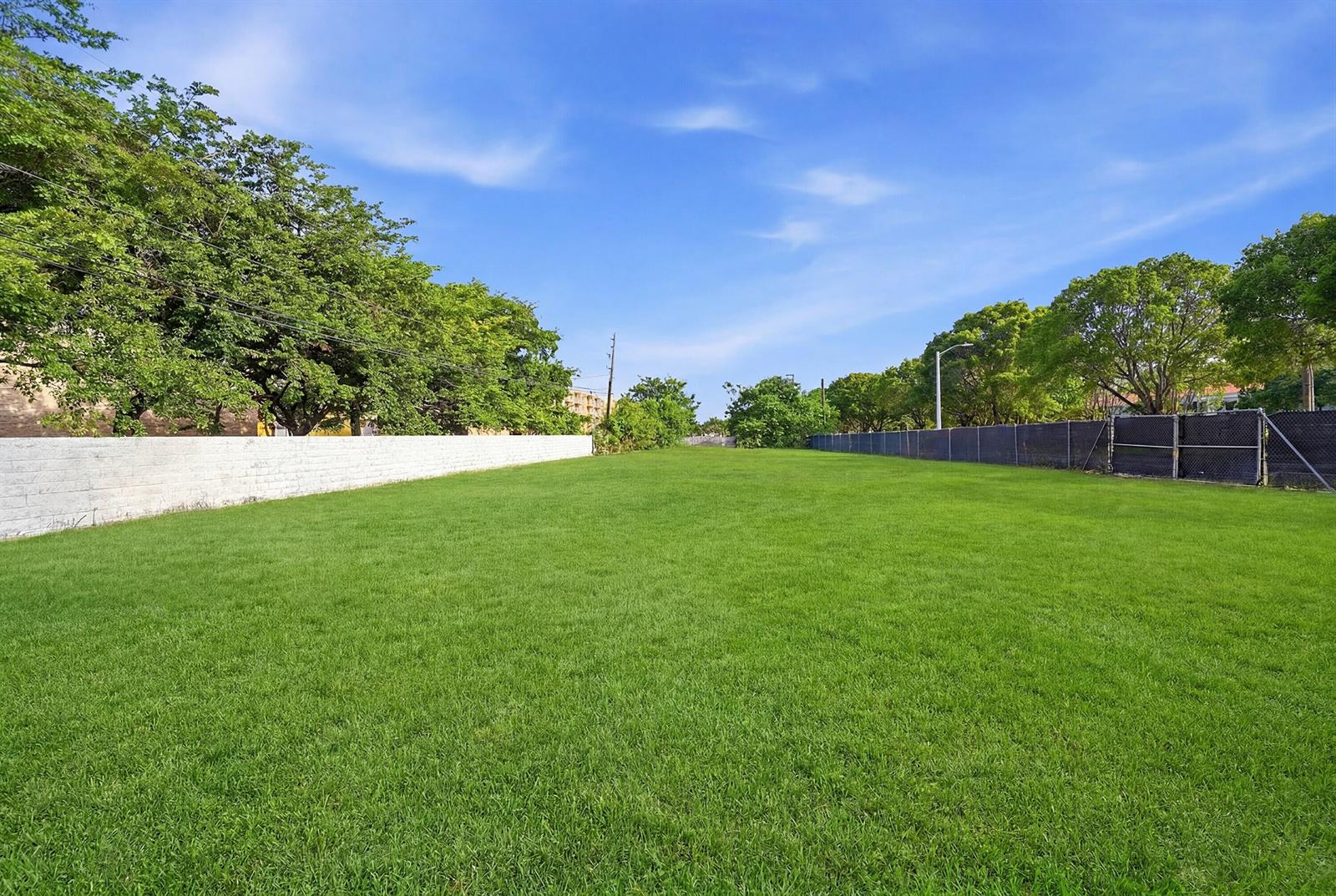 A large, rectangular grassy lot is enclosed by a white brick wall and chain-link fencing — 1800 N Sherman Circle, Miramar FL 33025, MIRAMAR, FL