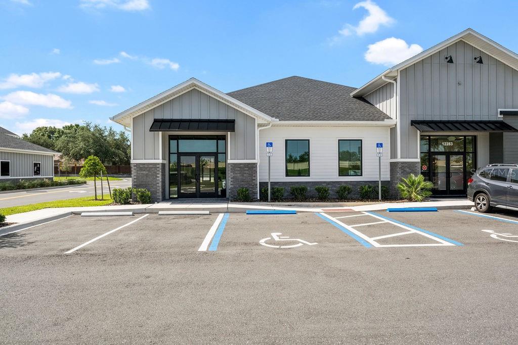 A modern commercial building with gray siding and two glass entrance doors faces a parking lot — 12283 STONEYBROOK WEST PARKWAY UNIT B, WINTER GARDEN, FL