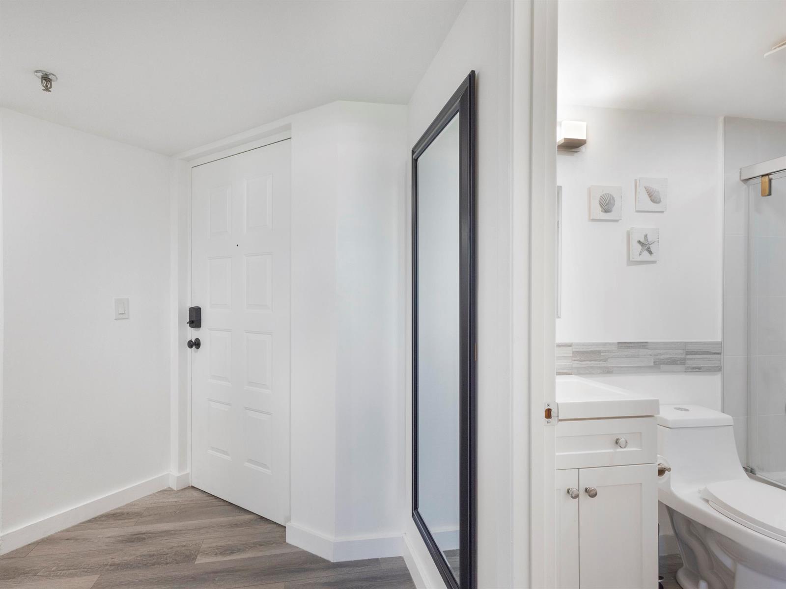 A white door and a full-length mirror stand next to a bathroom with white cabinetry — 955 Egret Circle # 402, Delray Beach FL 33444, DELRAY BEACH, FL