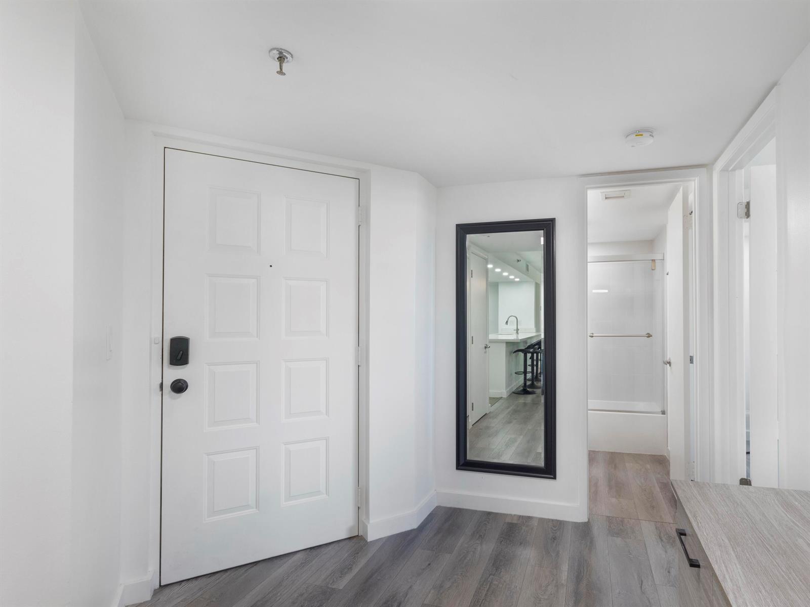 An entryway features a white door, a black-framed wall mirror, and light wood-look flooring — 955 Egret Circle # 402, Delray Beach FL 33444, DELRAY BEACH, FL
