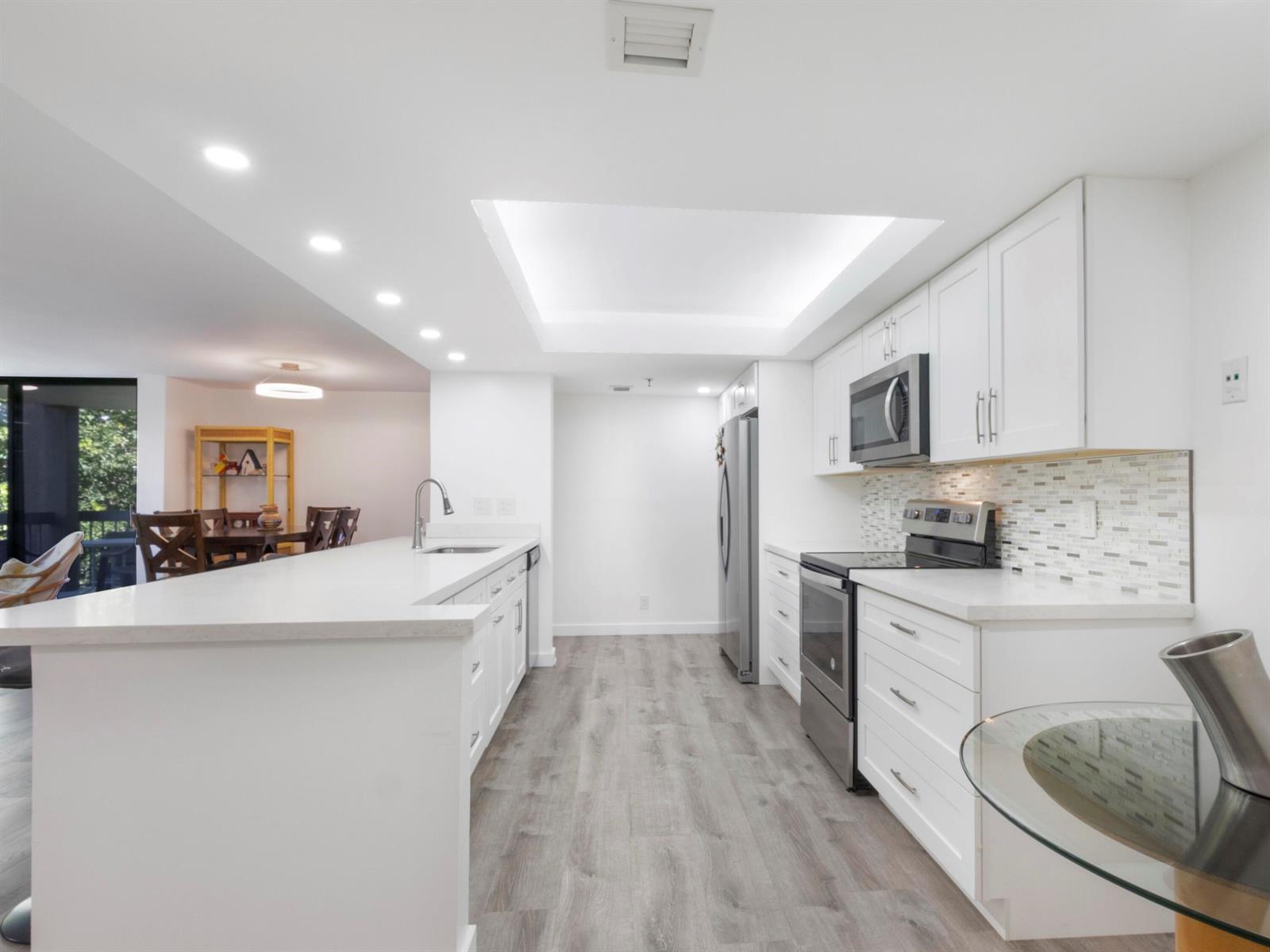 A modern white kitchen features a large island, stainless steel appliances, and wood-look flooring — 955 Egret Circle # 402, Delray Beach FL 33444, DELRAY BEACH, FL