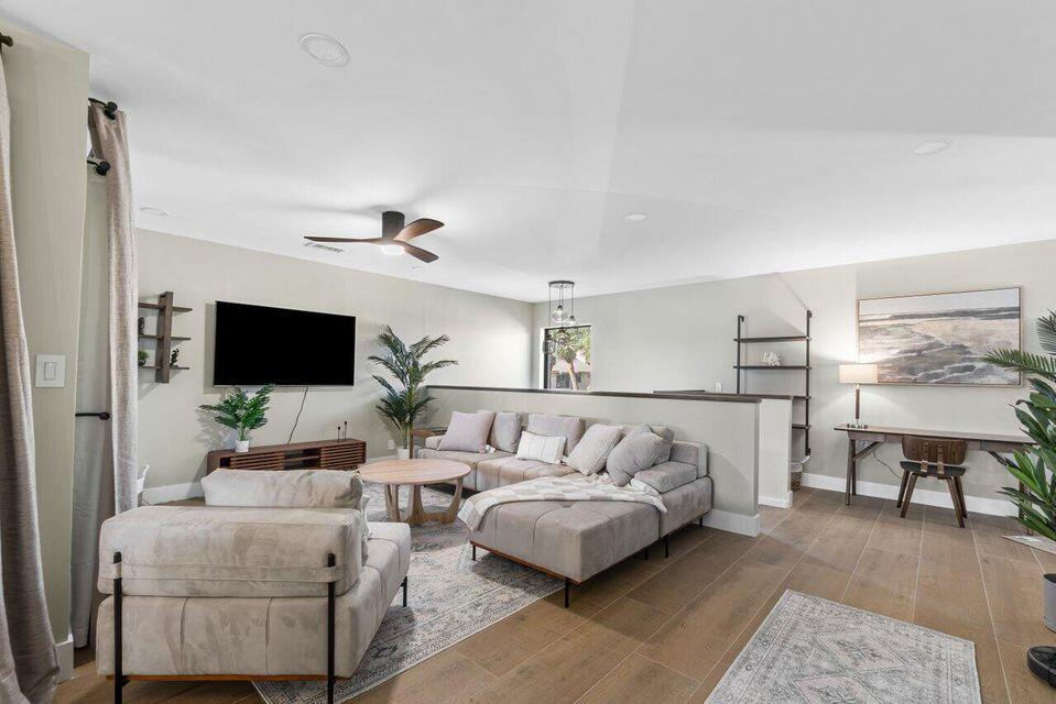 A living room features a sectional sofa, a television, and wood-look flooring — 17138 Waterbend Drive # 217, Jupiter FL 33477, JUPITER, FL