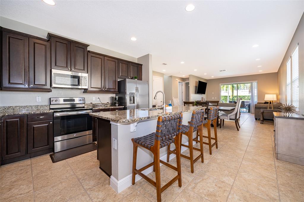 A kitchen with dark wood cabinets, granite countertops, and an island with three bar stools — 250 PENDANT COURT, KISSIMMEE, FL