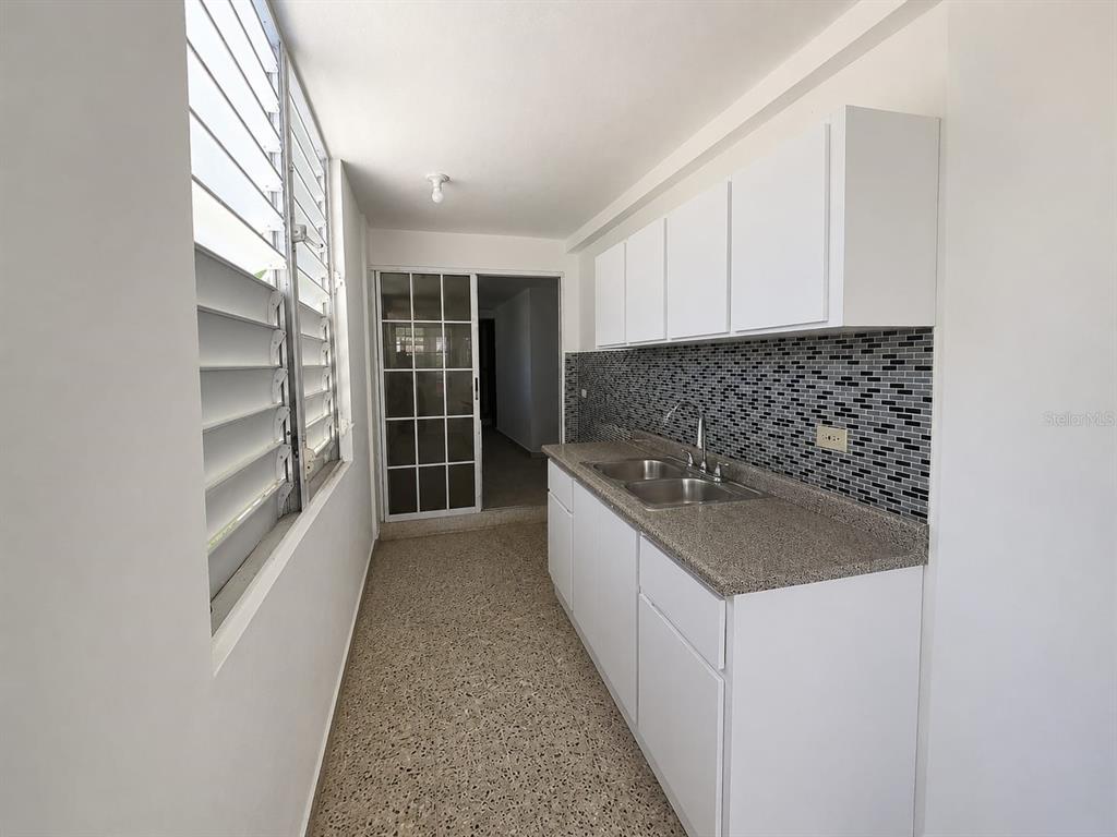 A narrow kitchen features white cabinets, a granite countertop, and a mosaic tile backsplash — A1A CALLE A  URB. LOS ANGELES, YABUCOA, PR