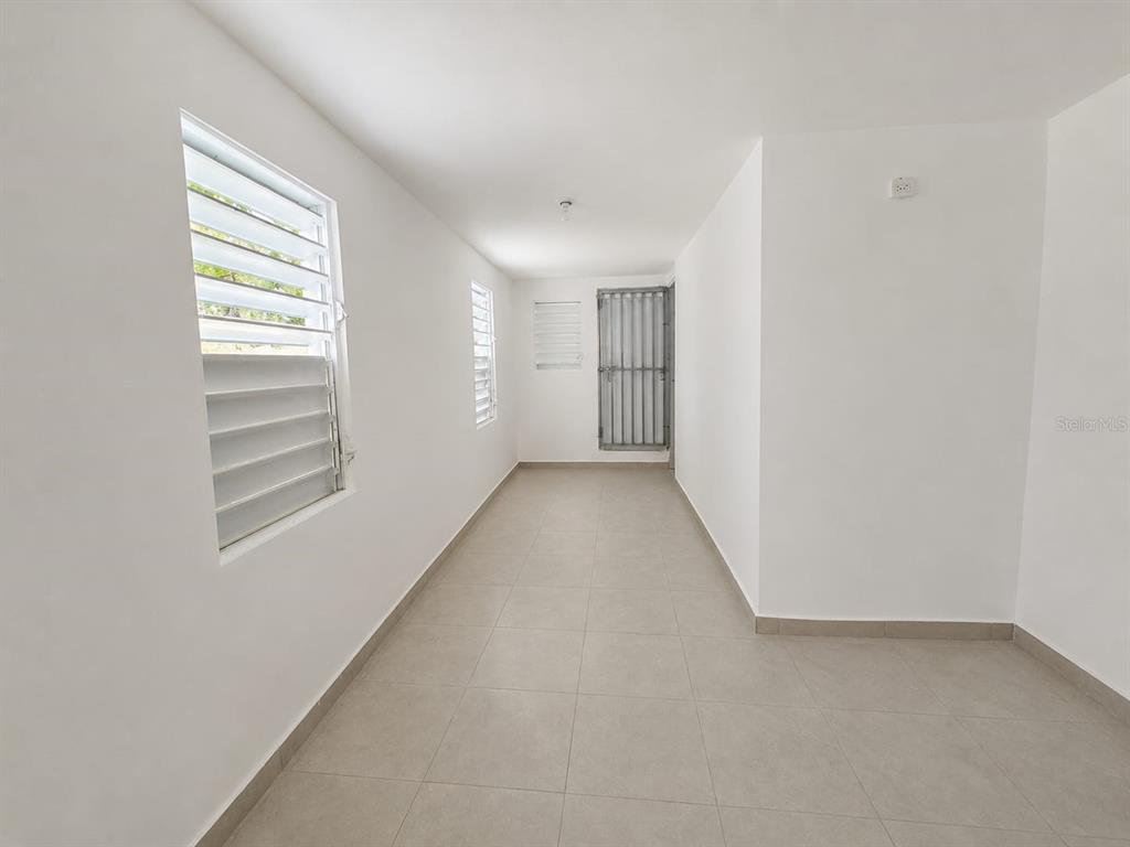 An empty room with white walls, tiled floors, and multiple windows with security bars — A1A CALLE A  URB. LOS ANGELES, YABUCOA, PR
