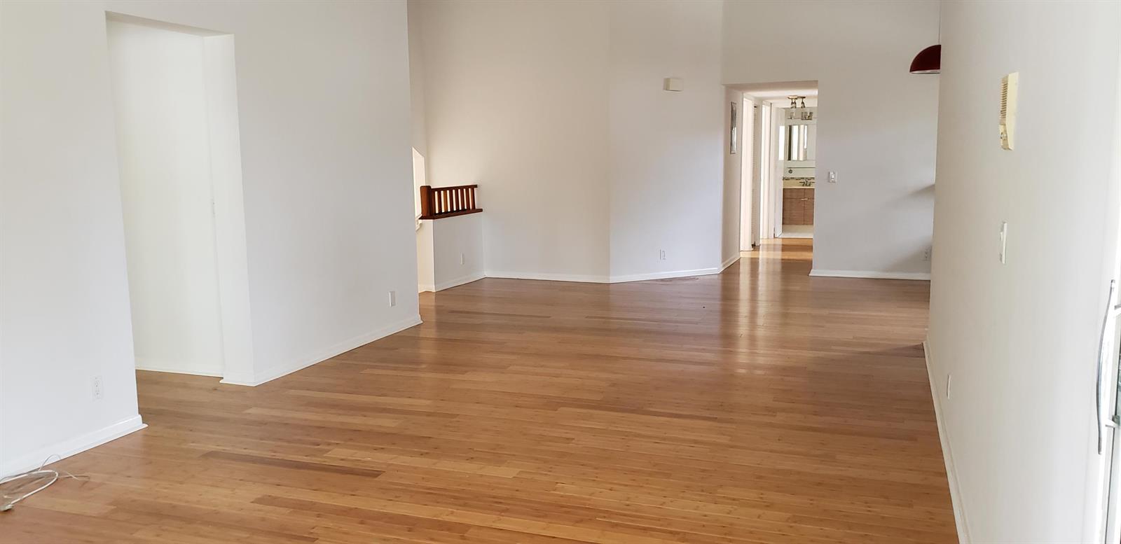 An empty room with light-colored walls and hardwood flooring features a staircase and doorway — 5326 Buckhead Circle # 2010, Boca Raton FL 33486, BOCA RATON, FL