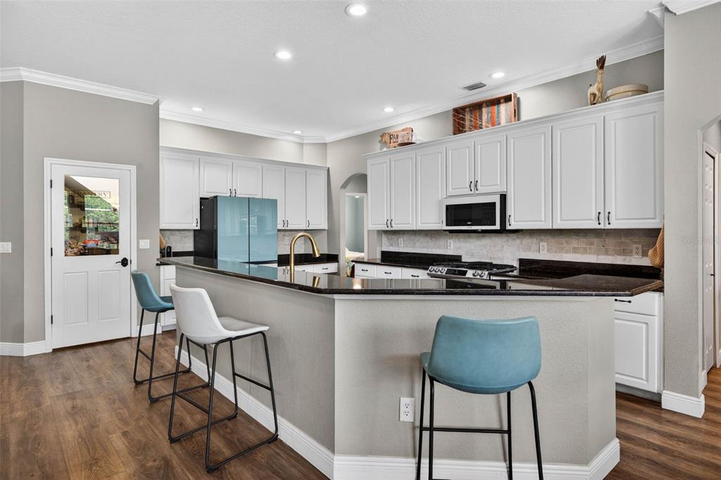 A kitchen with white cabinets, dark granite countertops, a breakfast bar, and three stools — 18127 HERON WALK DRIVE, TAMPA, FL