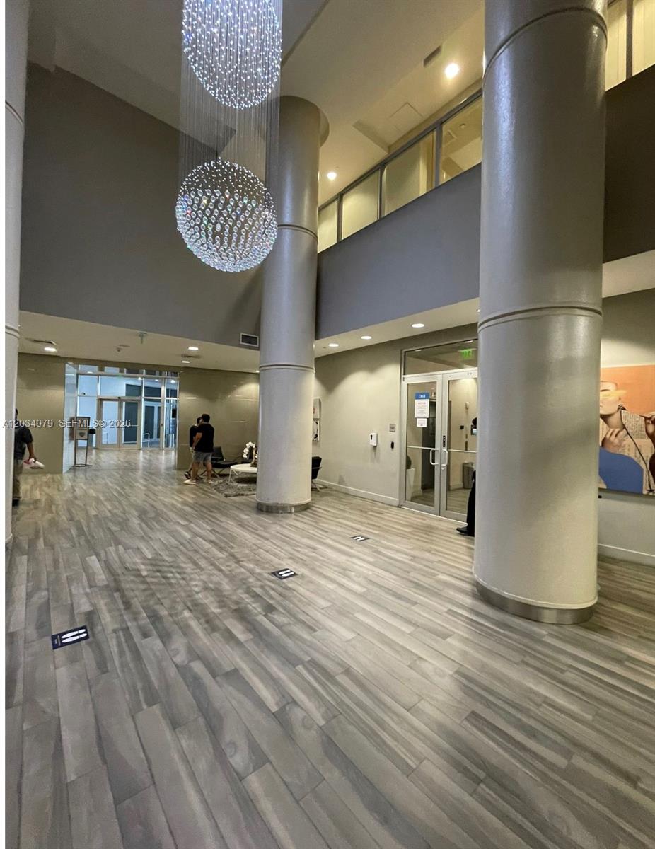 A modern building lobby features wood-look flooring, two large structural columns, and hanging crystal chandeliers — 1750 N Bayshore Dr # 3010, Miami FL 33132, MIAMI, FL