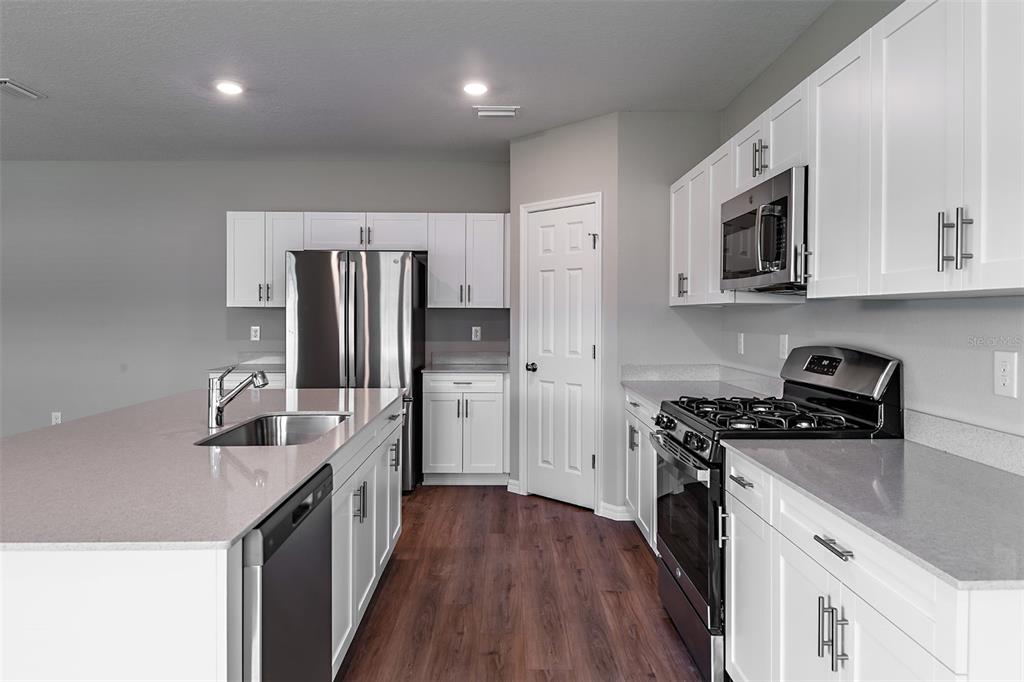 A modern kitchen features white cabinetry, stainless steel appliances, and a large quartz-topped island — 36672 SAGEMOOR DRIVE, ZEPHYRHILLS, FL