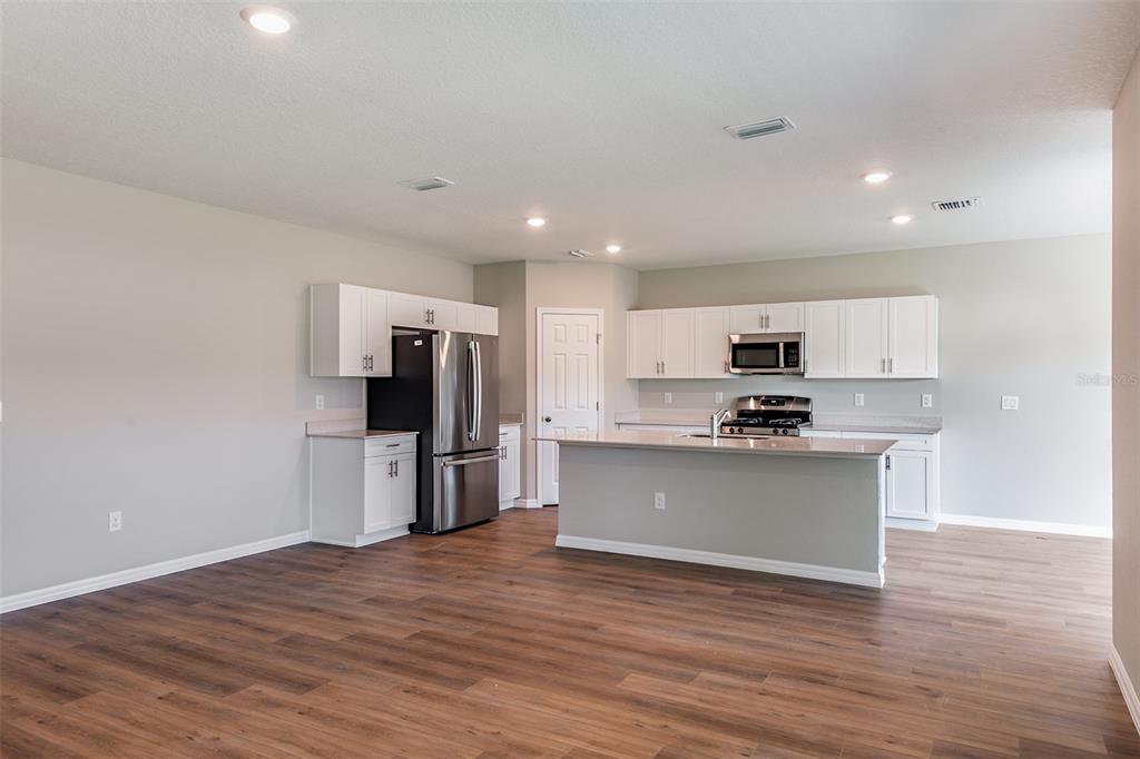 A kitchen features white cabinets, stainless steel appliances, a center island, and wood-look flooring — 36672 SAGEMOOR DRIVE, ZEPHYRHILLS, FL