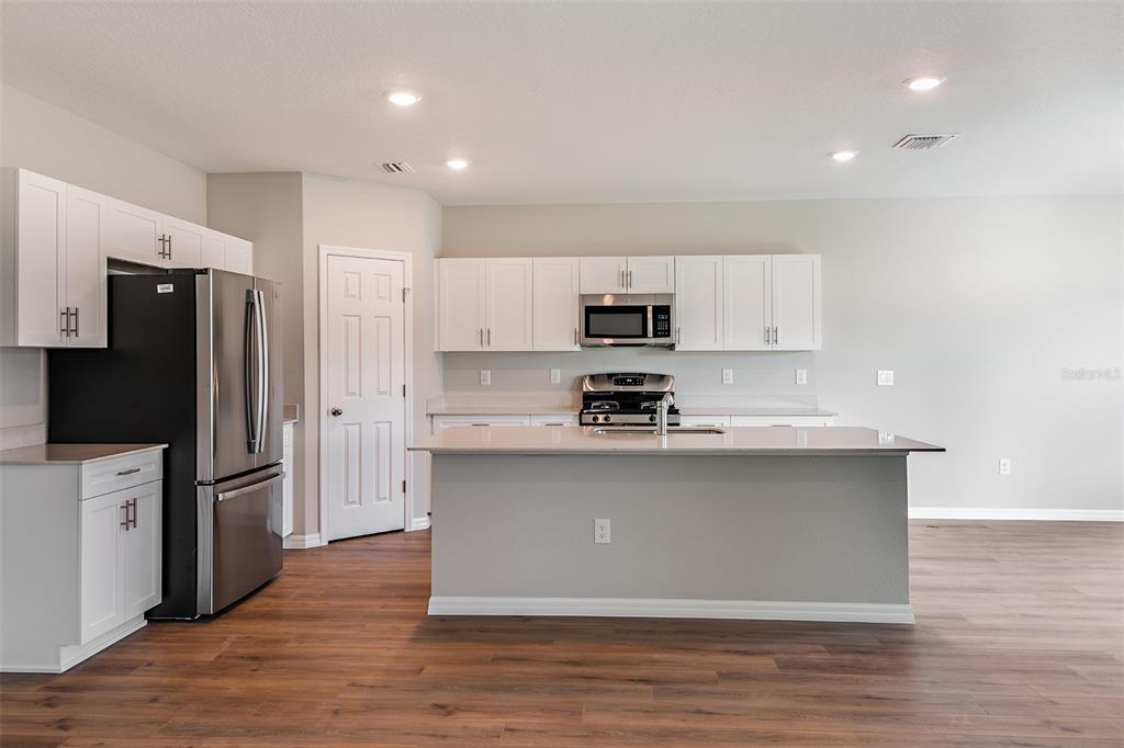 A kitchen with white cabinets, stainless steel appliances, a center island, and wood-look flooring — 36672 SAGEMOOR DRIVE, ZEPHYRHILLS, FL