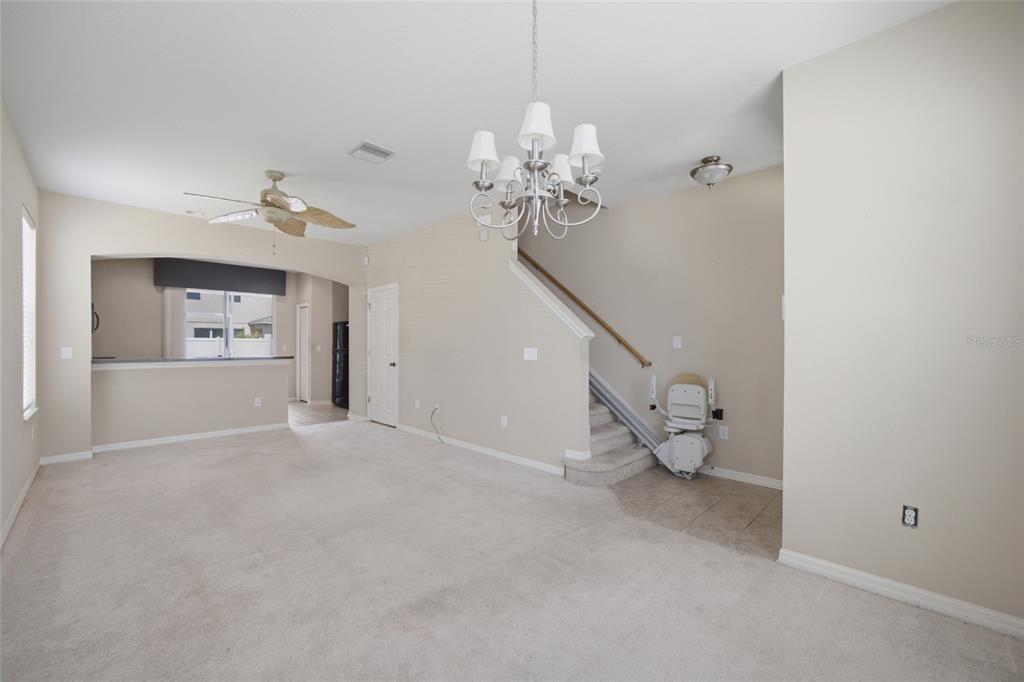 A living room with beige carpet, a chandelier, and a stairlift installed on the staircase — 6924 TOWERING SPRUCE DRIVE, RIVERVIEW, FL