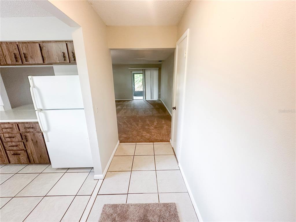 A kitchen with wood cabinets and a white refrigerator leads into a carpeted living area — 585 N SCENIC HIGHWAY UNIT 585, BABSON PARK, FL