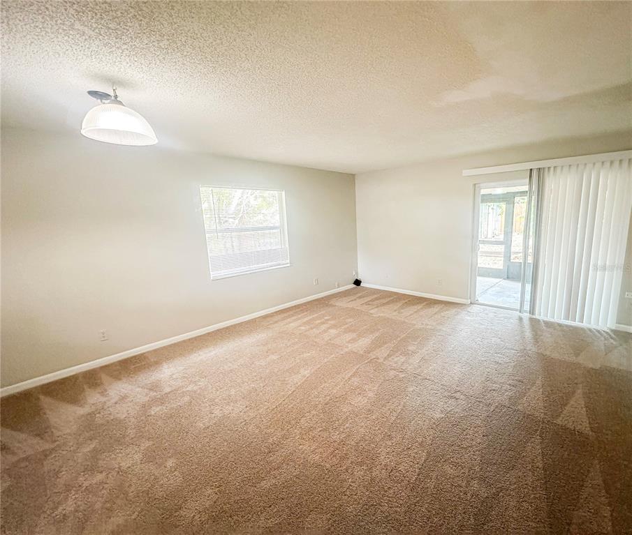 An empty living room with beige carpet, a single window, and a sliding glass door — 585 N SCENIC HIGHWAY UNIT 585, BABSON PARK, FL