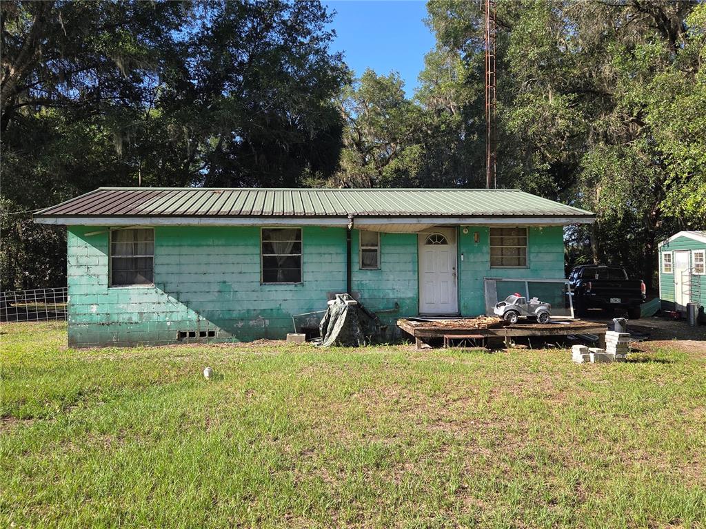 A single-story green house with a metal roof and a small wooden deck — 9845 NW 160TH STREET, REDDICK, FL