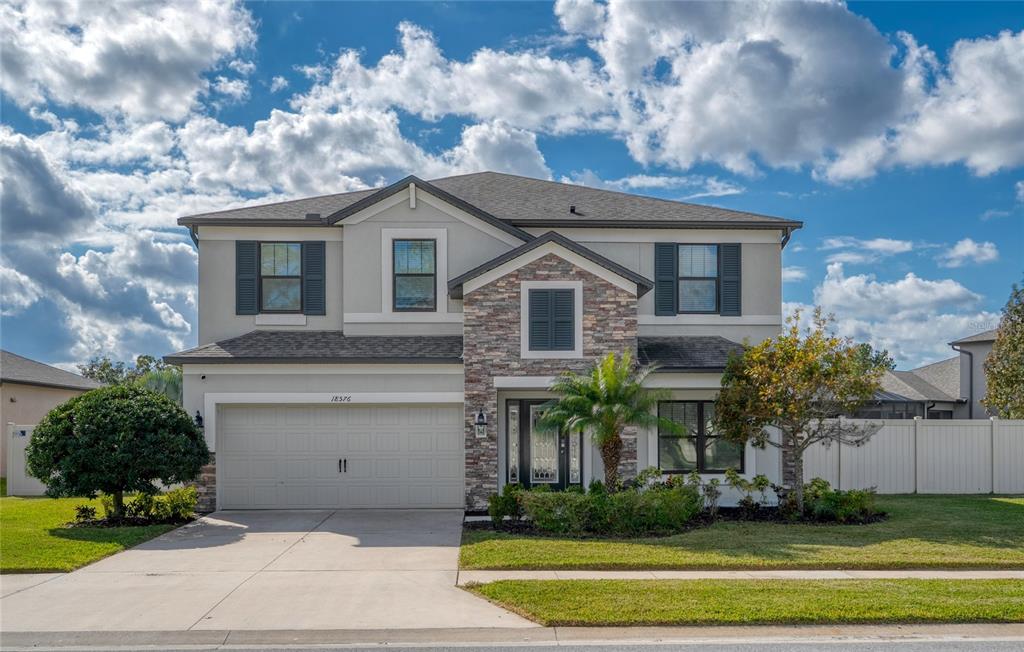 A two-story suburban house with a stone facade, garage, and a palm tree in front — 18576 OBREGAN DRIVE, SPRING HILL, FL
